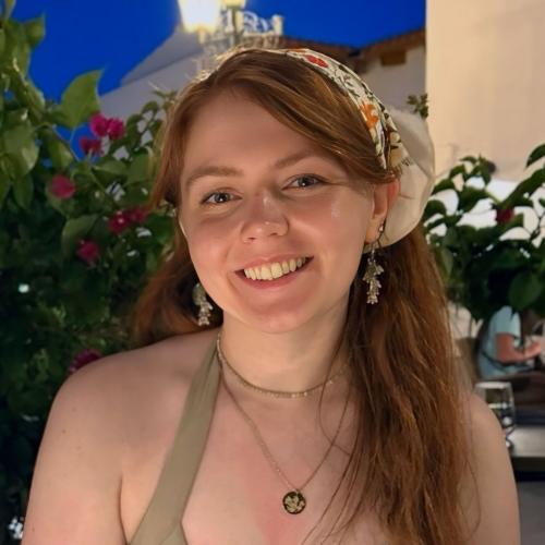 Headshot of a woman with red hair in front of a plant